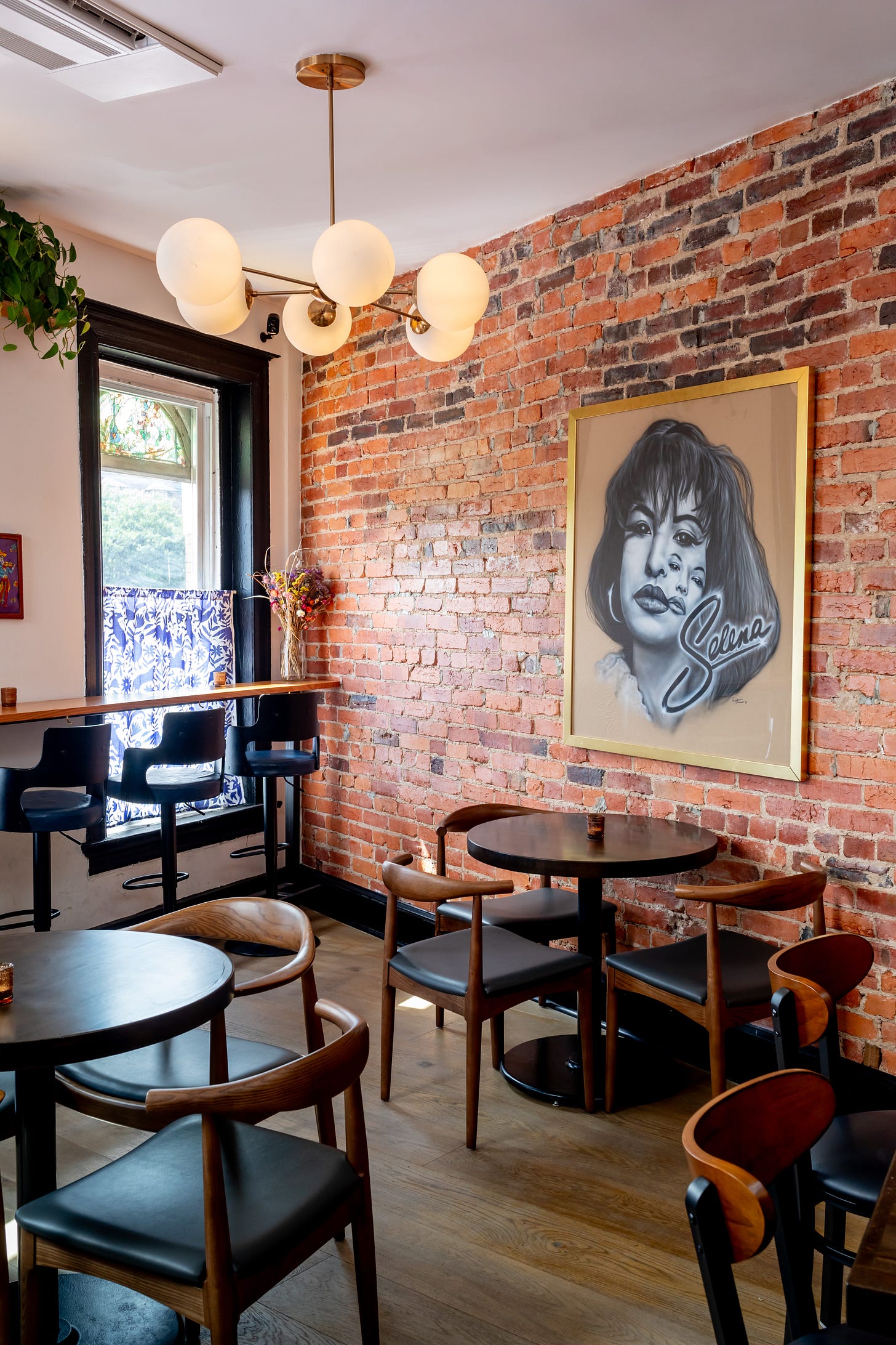 The upstairs bar space, with a brick wall, cocktail seating, and a portrait of Selena on the wall
