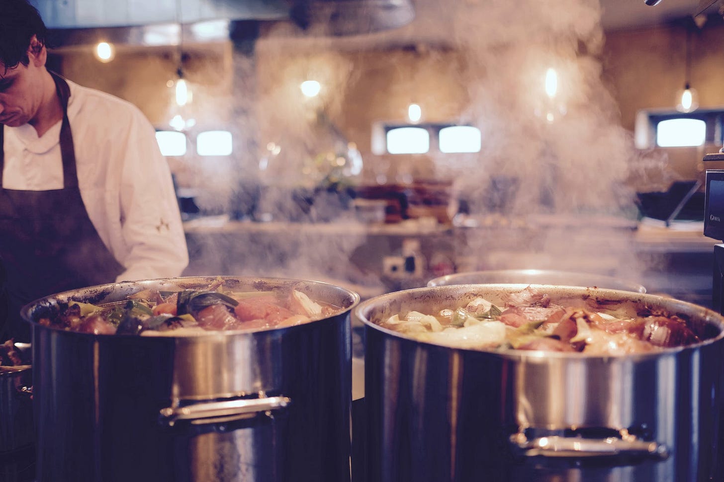 man wearing black apron near two silver metal cooking pot man wearing black apron near two silver metal cooking pot