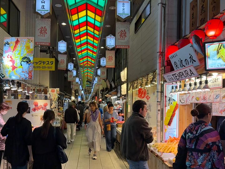 Left: the covered Nishiki market arcade in Kyoto, lined with food stalls. Right: two women sampling food at a market vendor.