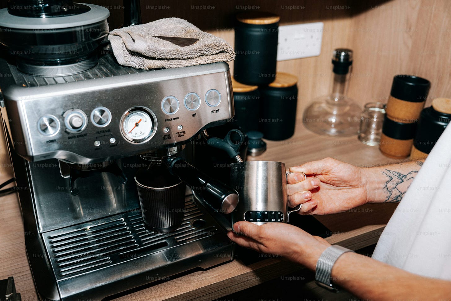 Barista steaming milk in a metal pitcher near espresso machine Barista steaming milk in a metal pitcher near espresso machine