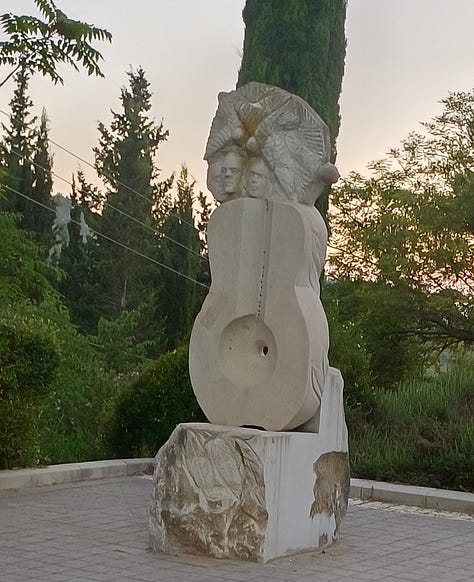Three large stone sculptures in front of the Bet Musika: a half-guitar/half-cello; a viol, and a guitar with the faces of three musicians surrounding the instrument's neck.