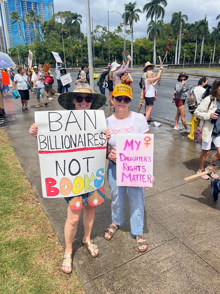 Protest signs that say "I can tell my kids I wasn't silent" and "ban billionaires not books"