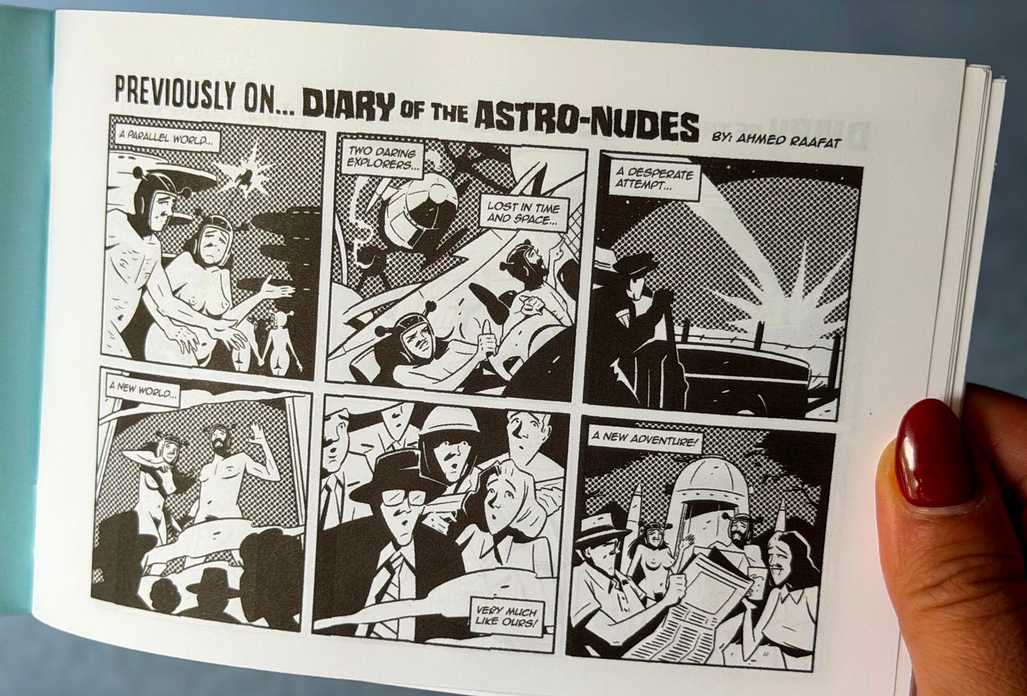A hand holds open a small black-and-white zine. The visible page shows a six-panel comic titled “Previously on… Diary of the Astro-Nudes” by Ahmed Raafat. The panels recap the story: Arr and Arreya exploring a parallel world, getting lost in time and space, making a desperate attempt to escape, arriving nude on 1950s Earth, surprising onlookers, and beginning a new adventure. The opposite page is printed on a pale blue sheet and is only partially visible.