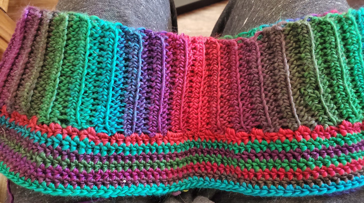 A crochet work in progress of shorts with stripes of greens, blues, and purples.