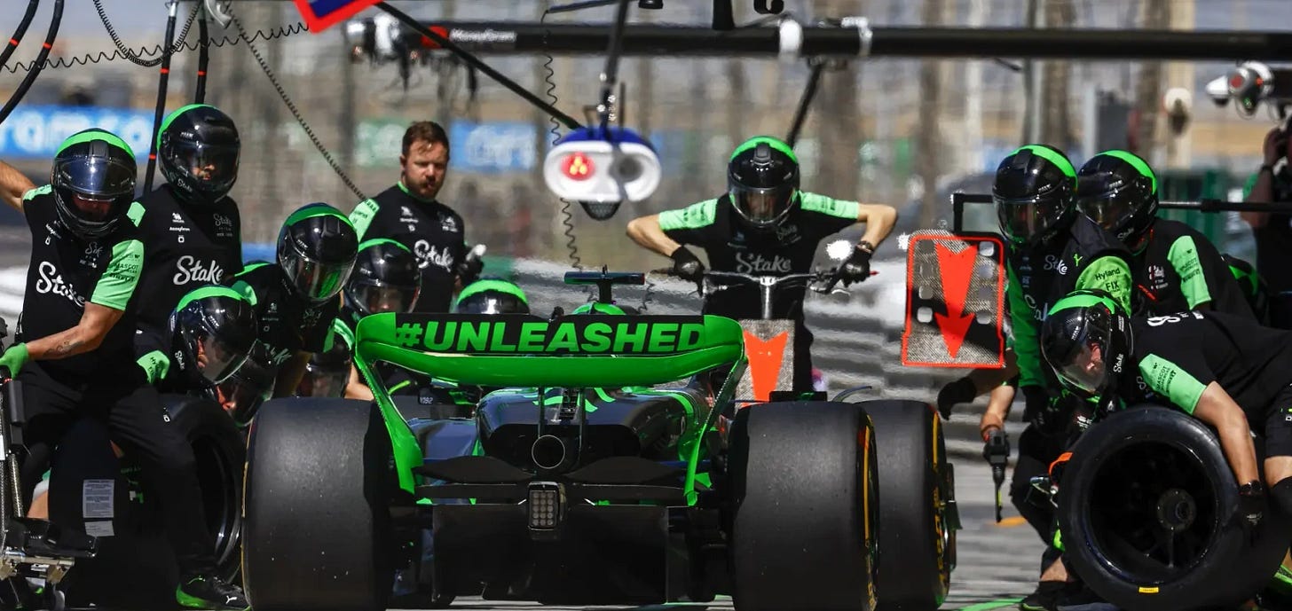 A pit stop practice looking from behind the car, the pit crew are caught pre swarm. Across the rear wing is "#unleashed" A pit stop practice looking from behind the car, the pit crew are caught pre swarm. Across the rear wing is "#unleashed"