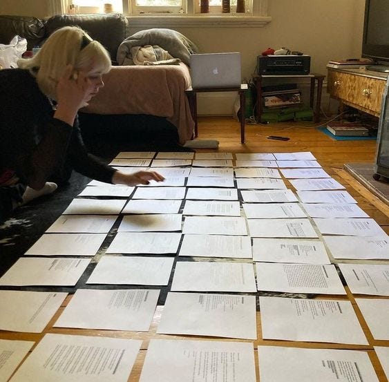 This may contain: a woman sitting on the floor surrounded by papers