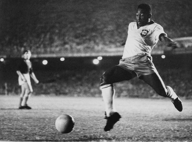 A footballer kicks the ball while an opponent looks on in the background. A footballer kicks the ball while an opponent looks on in the background.