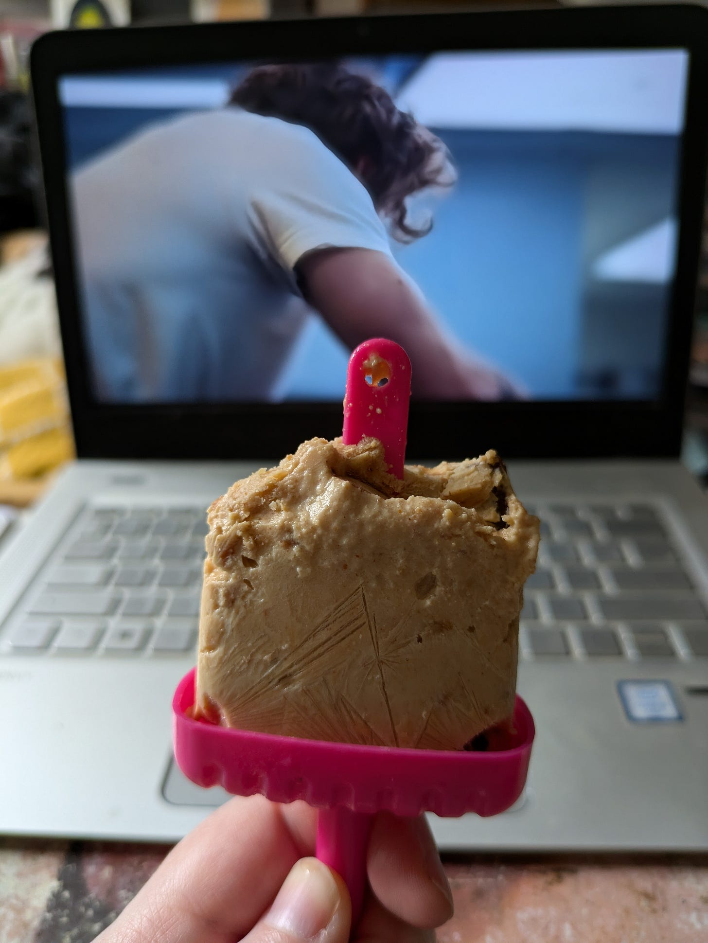 ID. Foreground - a half eaten frozen vegan peanut butter yoghurt treat on a pink ice lolly mould. Background - laptop and on the screen is a hilarious angled shot that looks like it is entirely focusing on Carmy’s tricep muscle as he leans over a counter. ID. Foreground - a half eaten frozen vegan peanut butter yoghurt treat on a pink ice lolly mould. Background - laptop and on the screen is a hilarious angled shot that looks like it is entirely focusing on Carmy’s tricep muscle as he leans over a counter.