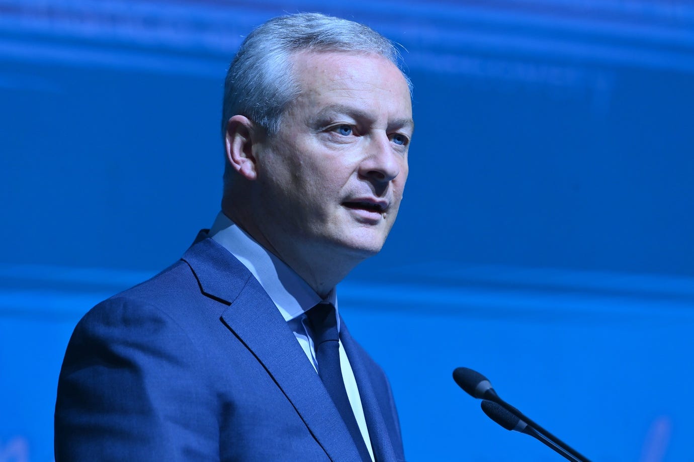 A person in a suit and tie standing in front of a microphone
Description automatically generated