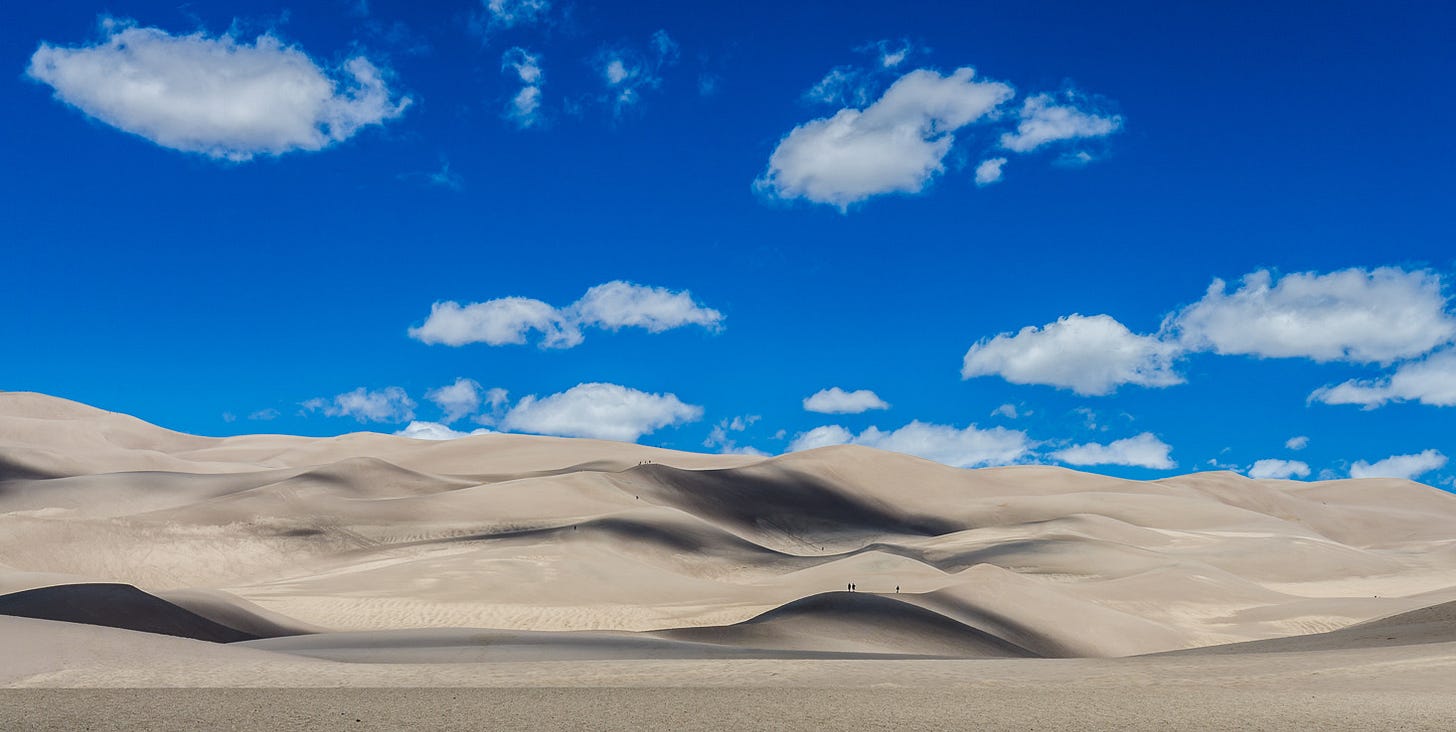 Sand dunes below a blue sky with clouds.