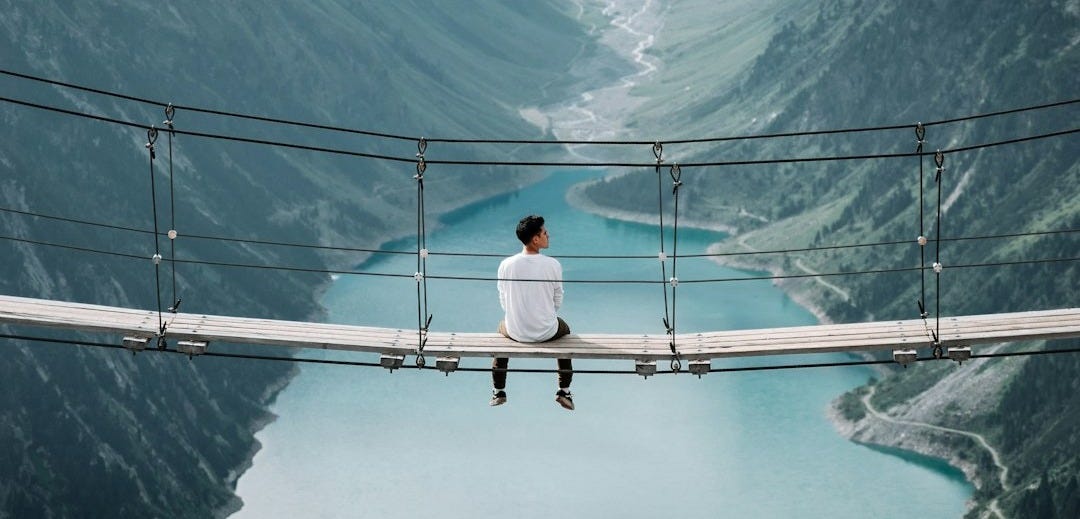 man wearing white shirt siting on bridge overlooking at mountain man wearing white shirt siting on bridge overlooking at mountain