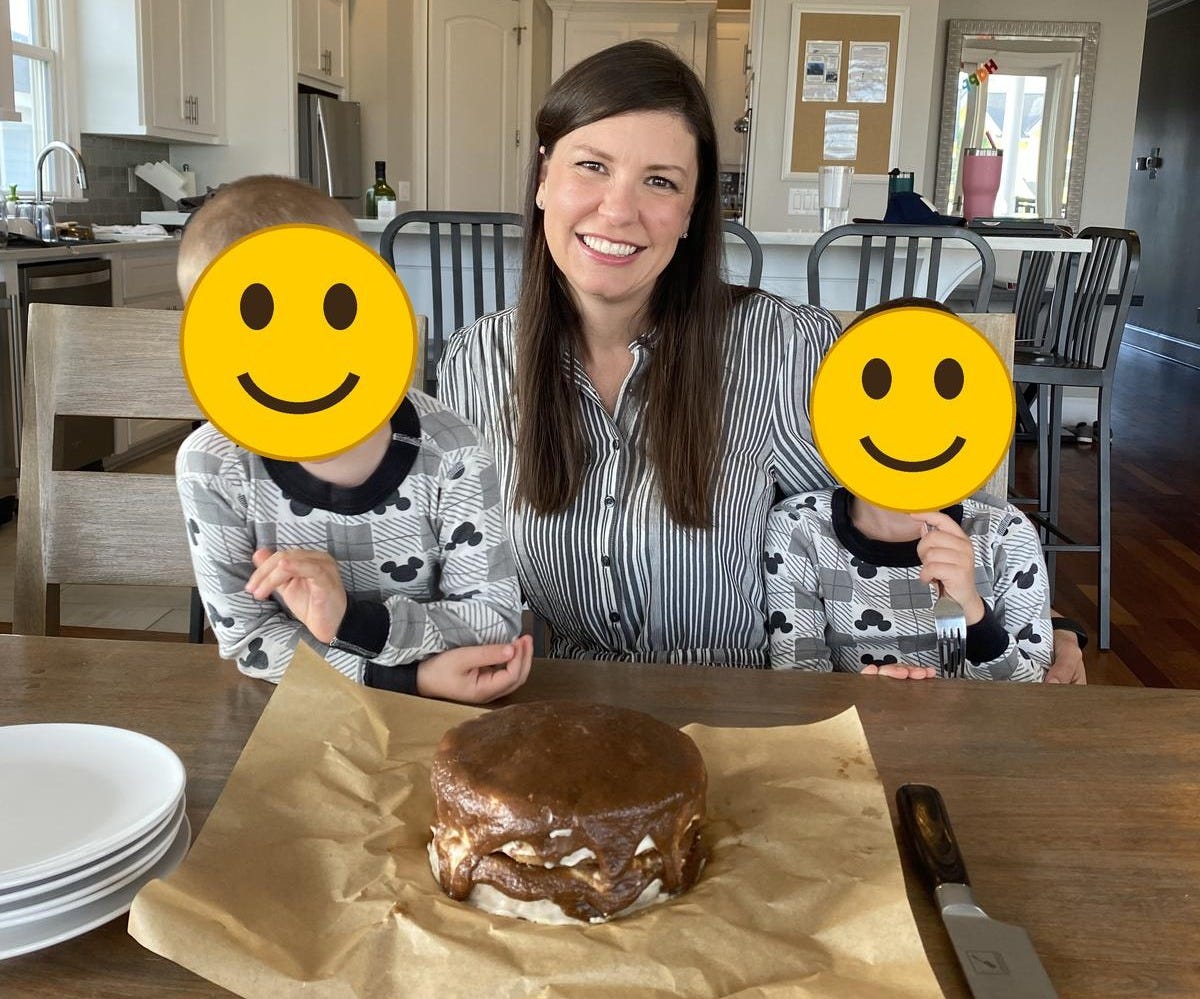 Kristen smiling at a kitchen table between her two young sons in matching Mickey Mouse pajamas, with a chocolate-frosted layer cake on parchment paper in front of them. Smiley faces cover the boys’ faces. Kristen smiling at a kitchen table between her two young sons in matching Mickey Mouse pajamas, with a chocolate-frosted layer cake on parchment paper in front of them. Smiley faces cover the boys’ faces.