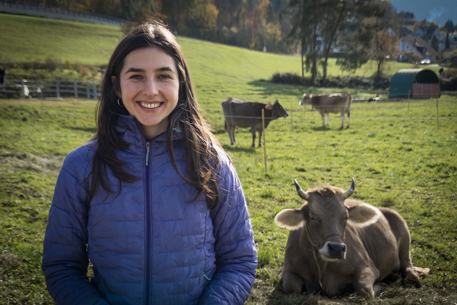 Jasmin Hufschmid von Bio Suisse steht lächelnd auf einer grünen Weide. Im Hintergrund sind Original Braunvieh-Kühe, Bäume mit herbstlicher Färbung und die sanft hügelige Landschaft des Mittellands zu sehen. Jasmin Hufschmid von Bio Suisse steht lächelnd auf einer grünen Weide. Im Hintergrund sind Original Braunvieh-Kühe, Bäume mit herbstlicher Färbung und die sanft hügelige Landschaft des Mittellands zu sehen.
