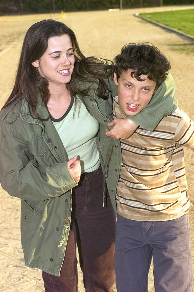 This may contain: two young people standing next to each other on a dirt road with trees in the background