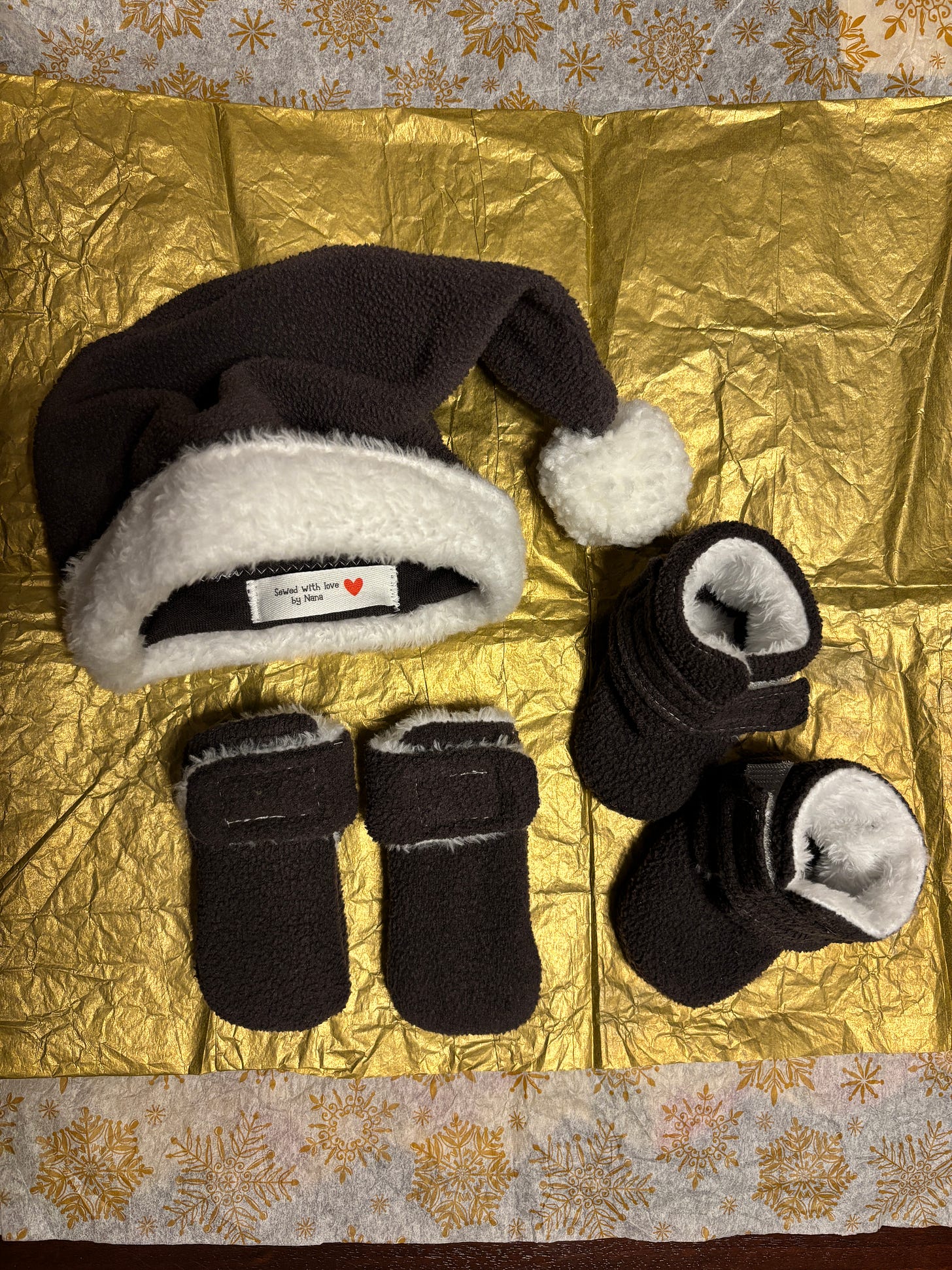 A homemade baby hat, booties, and mittens in dark grey fleece with white trim.
