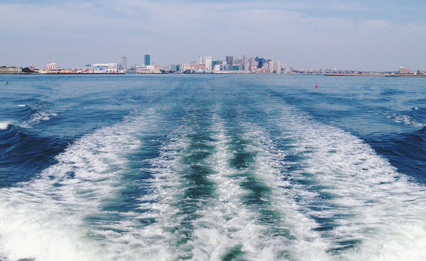 The wake of a boat in water with a small distant city sky line.