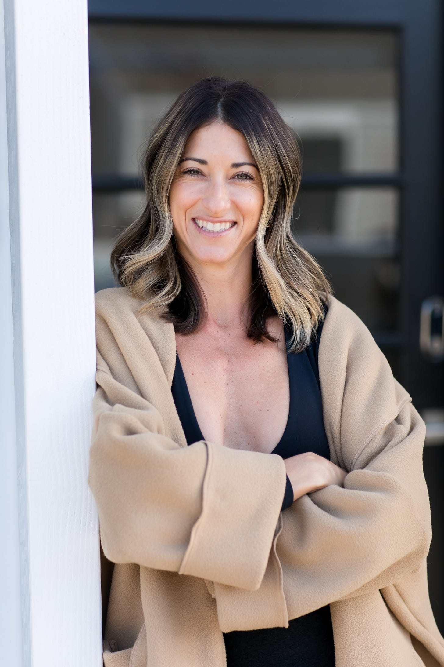 Vas Priebe standing outside her studio leaning on the pillar. Arms are crossed wearing a camel jacket.