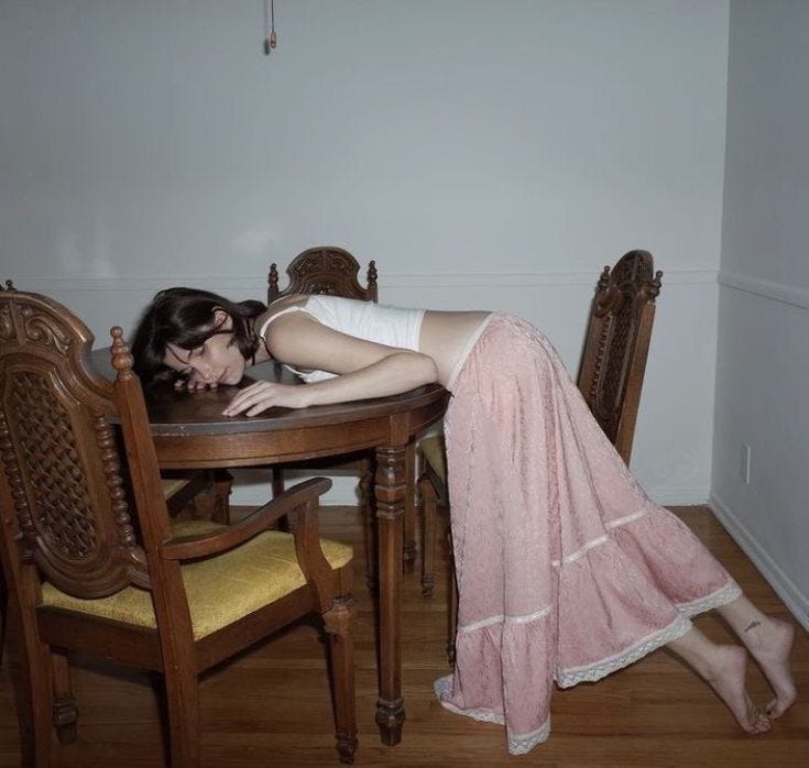 This may contain: a woman leaning over a wooden table with her head on the top of a chair