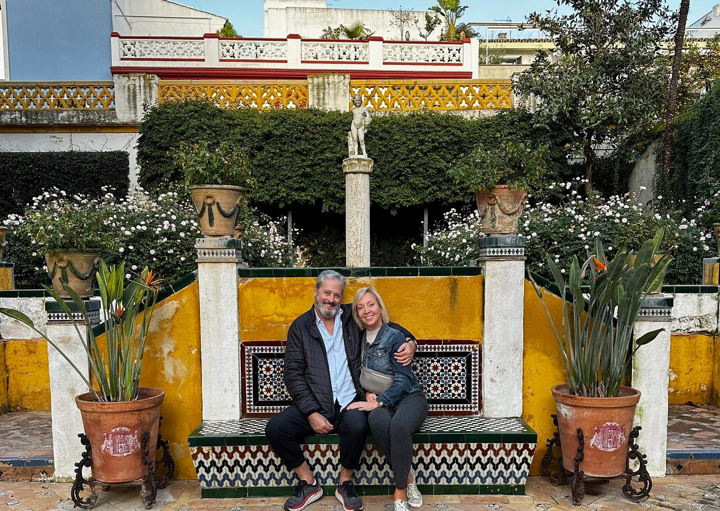 Kelly and Nigel Benthall sitting together on a colorful tiled bench in Seville, Spain, during their slow-travel gap year.