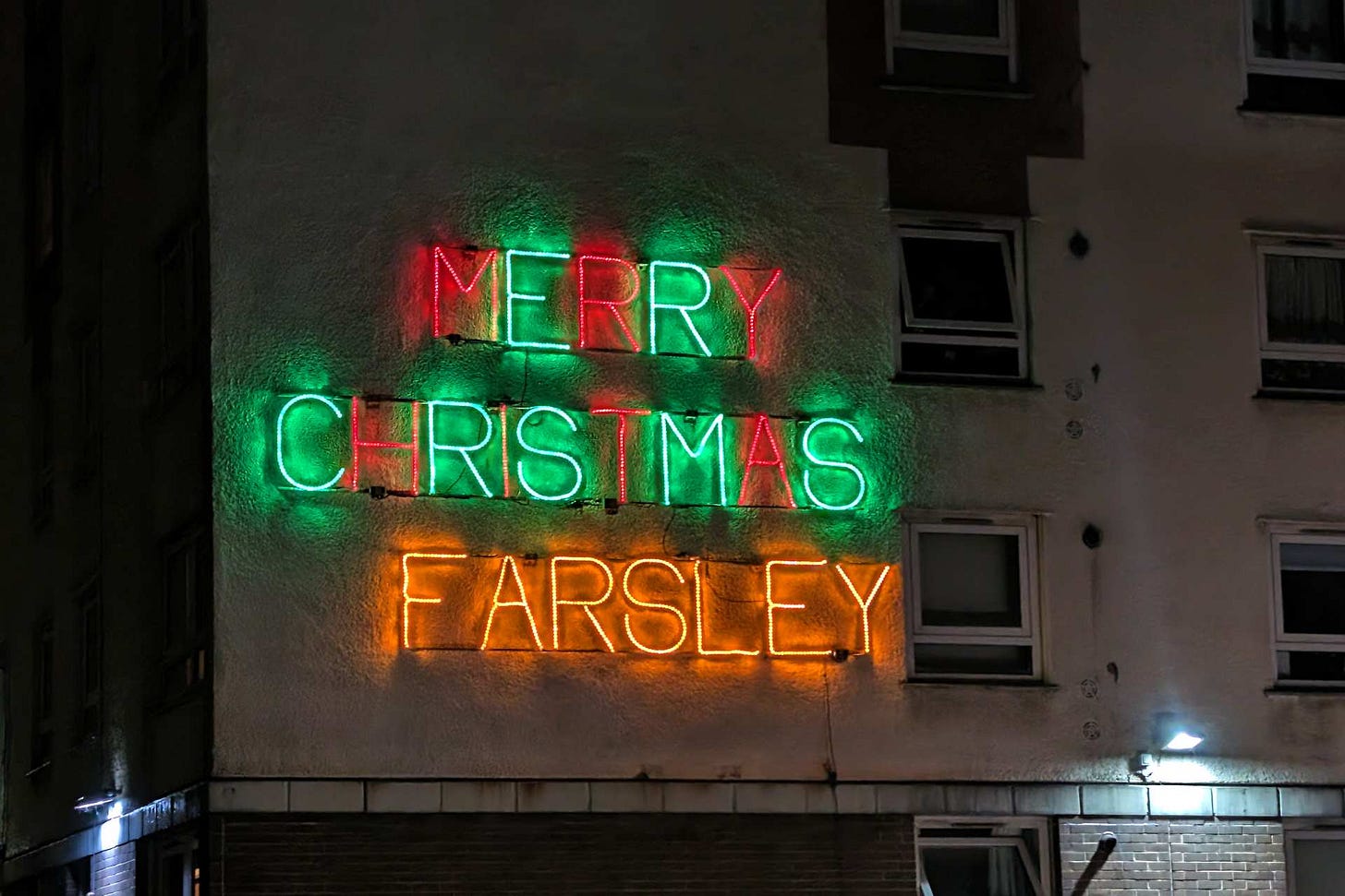 A neon light on the side of a tower block that reads "MERRY CHRISTMAS FARSLEY"