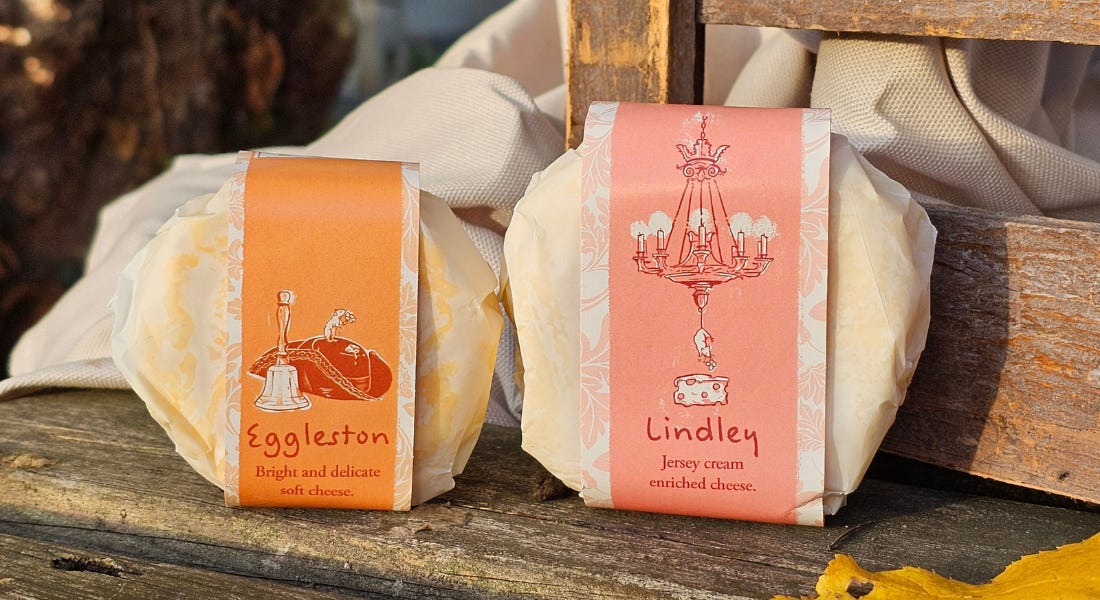 Two cheeses - one with an orange wrapper and one with pink - propped up on a bench Two cheeses - one with an orange wrapper and one with pink - propped up on a bench