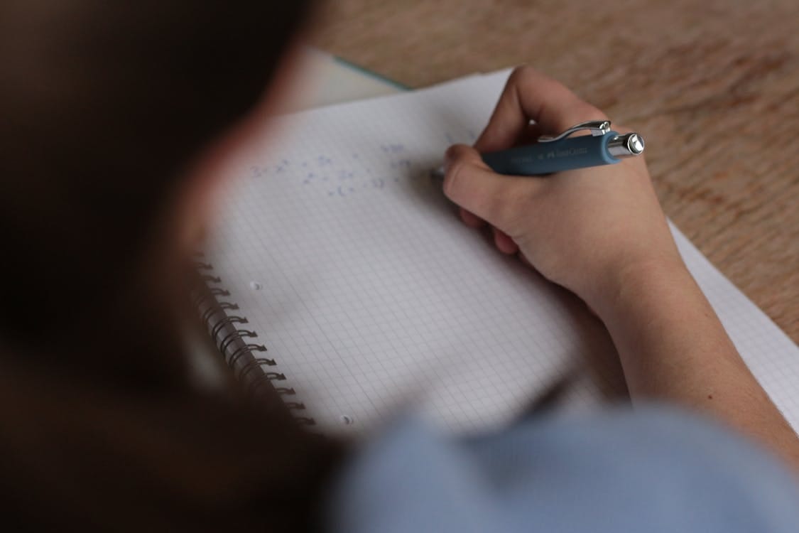 Free A student writes mathematical notes in a notebook using a pen, focus on studying. Stock Photo