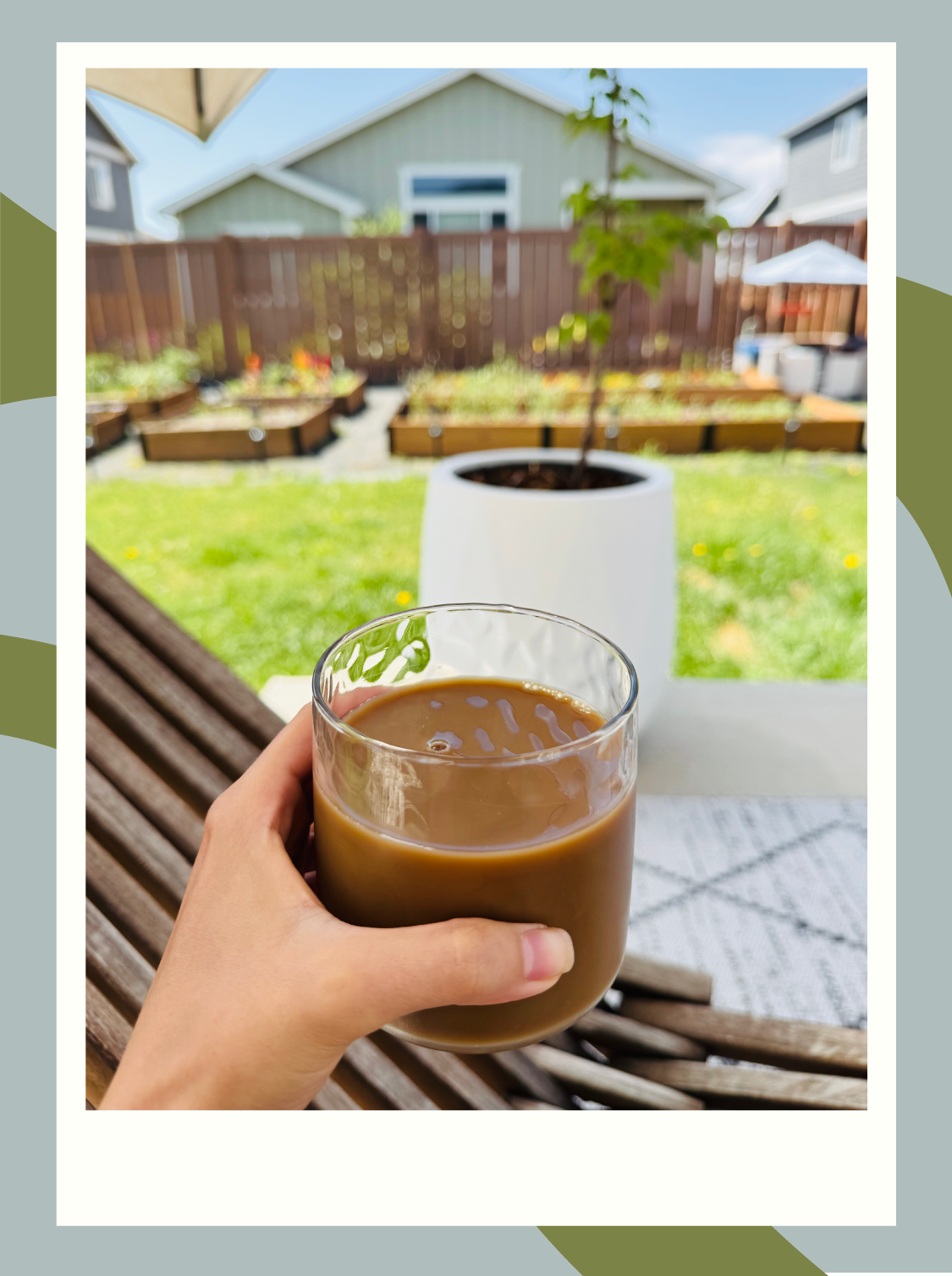 iced coffee in a clear glass cup in front of a backyard garden