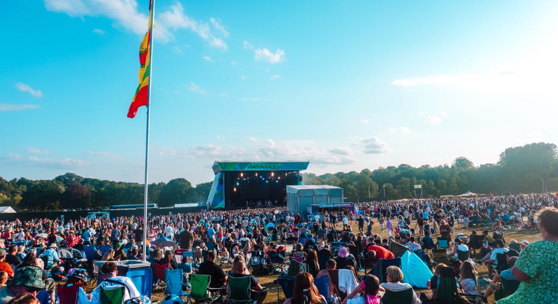 A large festival with a stage and a crowd of people in front A large festival with a stage and a crowd of people in front