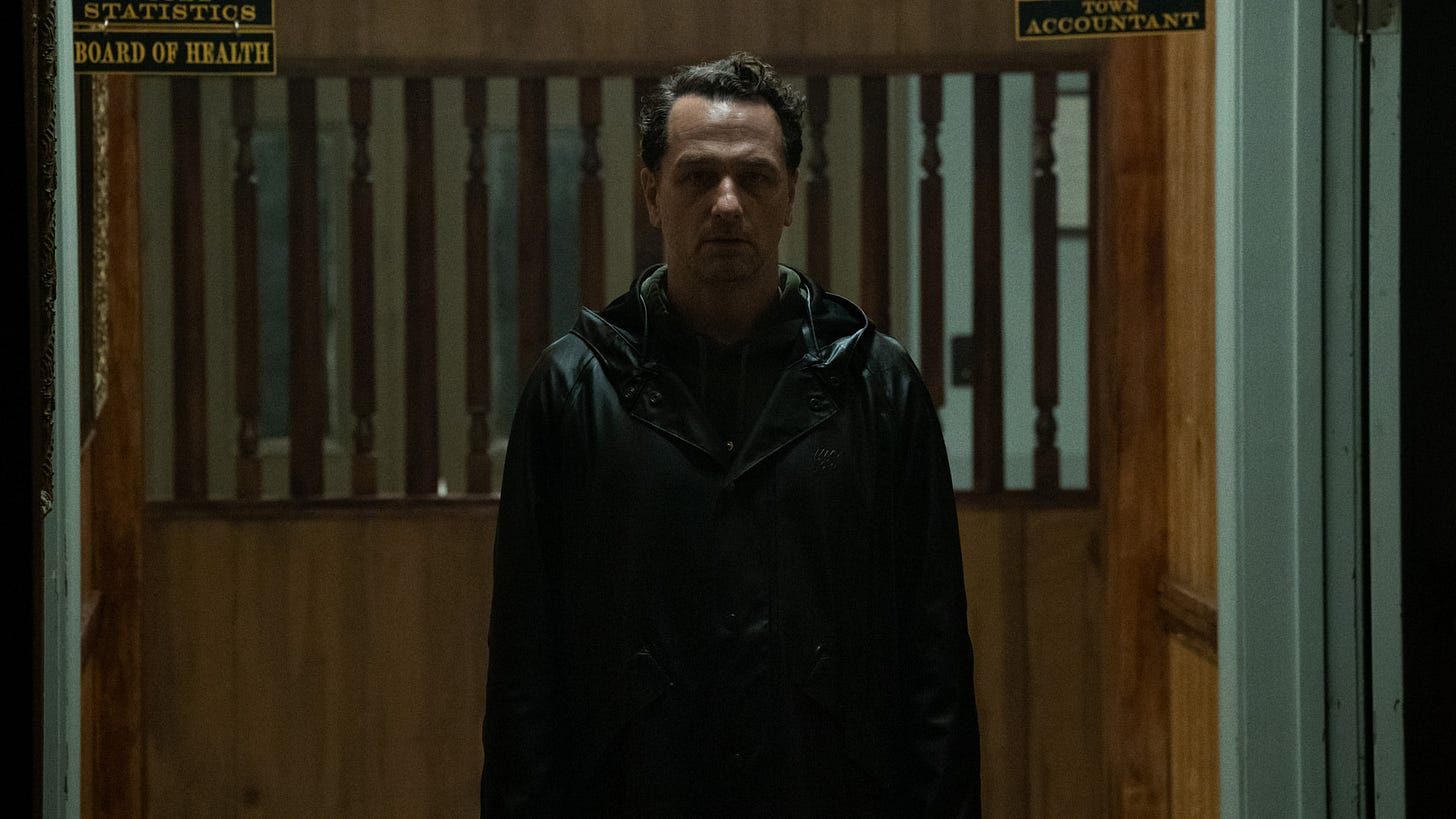 A still from a scene, showing the main character staring down a dim hallway towards the camera.