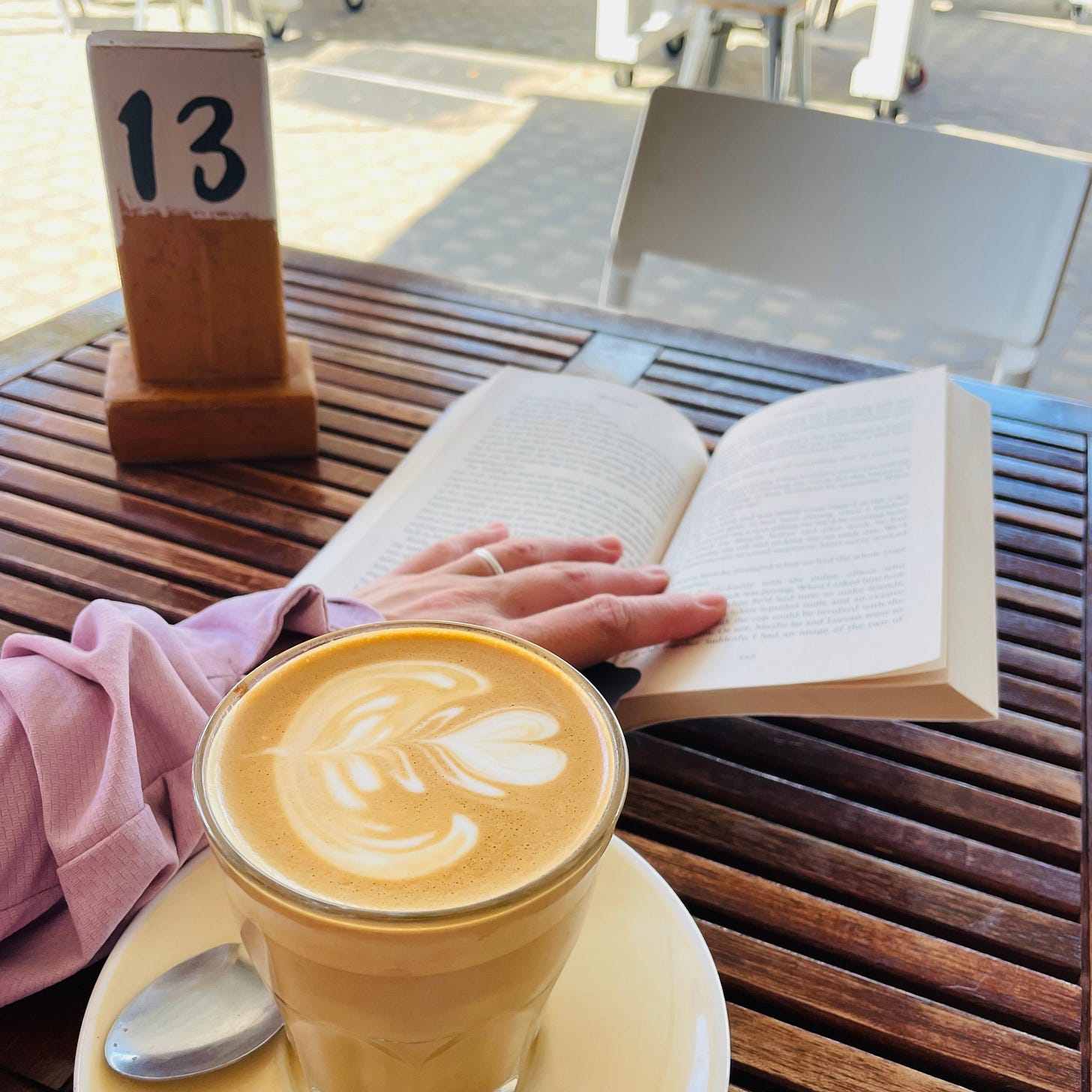 Miri is reading a book in a cafe setting with a coffee ready to sip in front of her