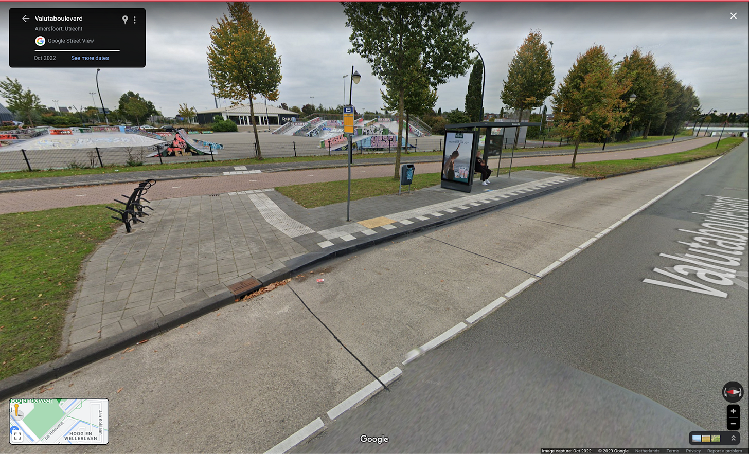 A bus stop, from the perspective of the roadway, showing a transit shelter, well marked platform, bike racks, garbage can and sidewalk.