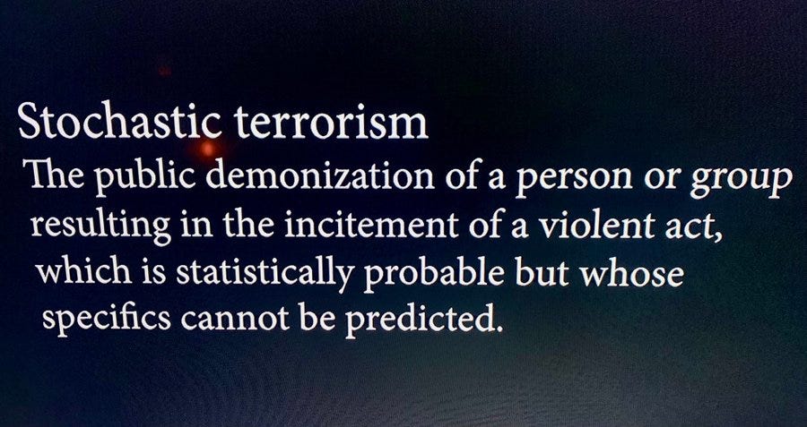 Text on a dark background reading "Stochastic terrorism. The public demonization of a person or group resulting in the incitement of a violent act, which is statistically probable but whose specifics cannot be predicted."