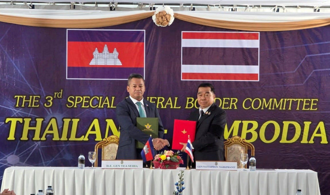 Cambodian Defense Minister Tea Seiha and Thai Defense Minister Nattaphon Narkphanit shake hands while holding a ceasefire agreement document in front of a backdrop depicting the flags of both countries.