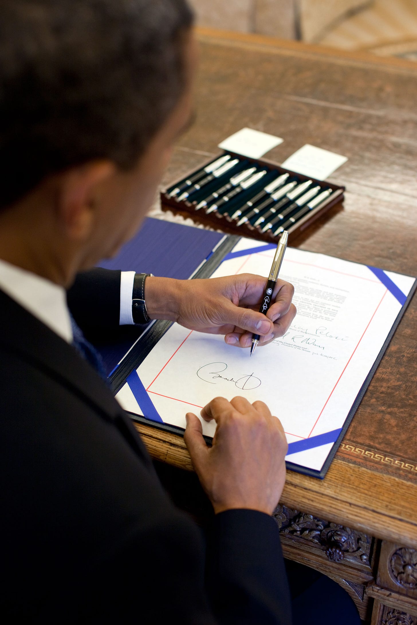 https://upload.wikimedia.org/wikipedia/commons/8/85/President_Barack_Obama_signs_a_bill_in_the_Oval_Office%2C_on_Aug._7%2C_2009.jpg
