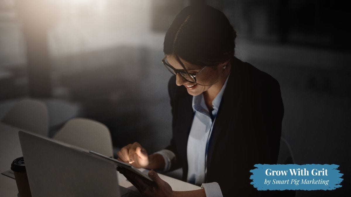 A business professional smiles while working on a tablet at a desk in a softly lit office. The image represents responsive customer service, professionalism, and thoughtful communication that help customers feel confident and supported. Grow With Grit by Smart Pig Marketing branding appears in the lower right corner.