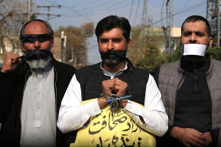 Three men protest with covered mouths, eyes and chained wrists. Three men protest with covered mouths, eyes and chained wrists.
