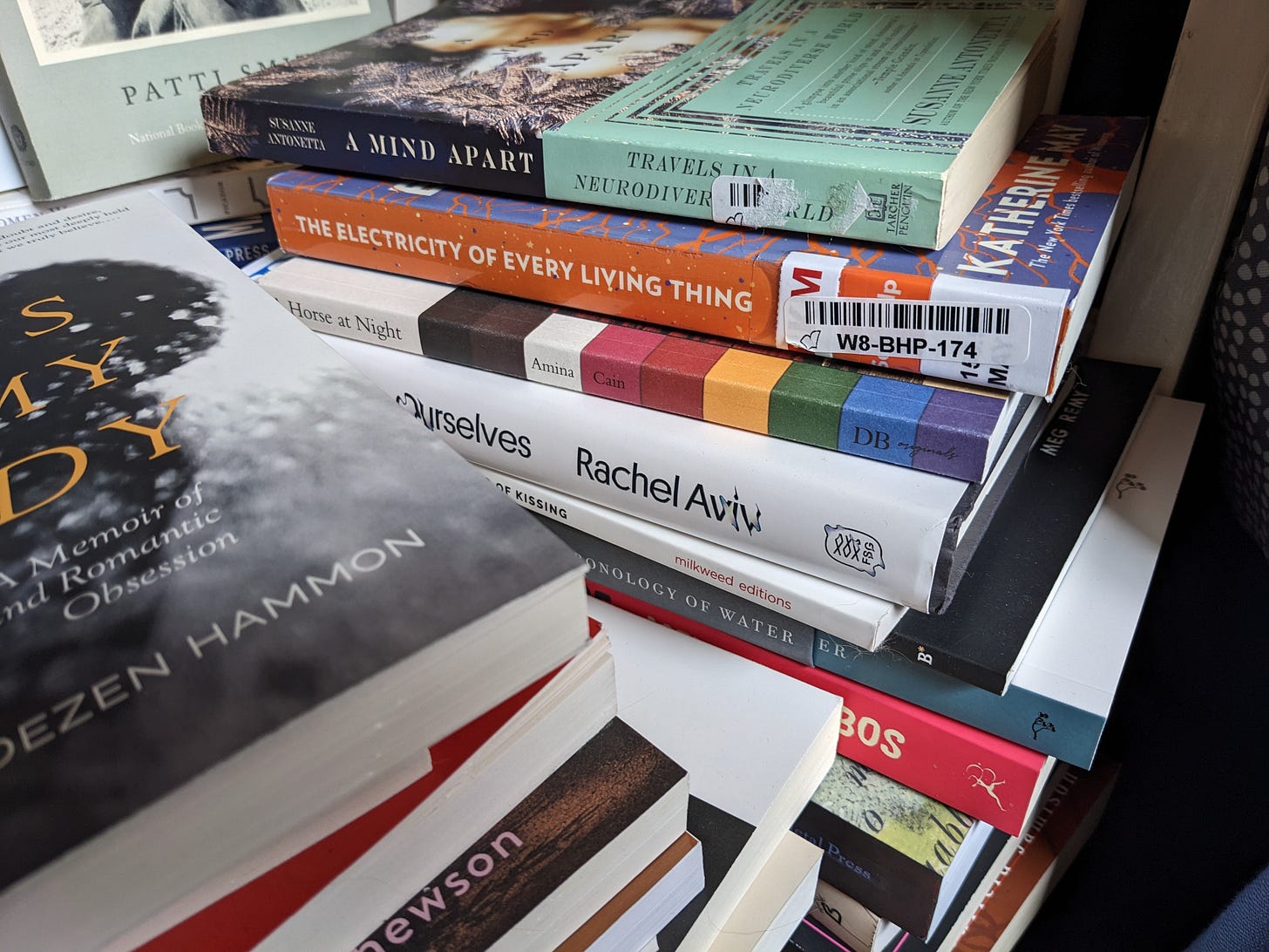 A few stacks of various books on my chair. Books include: A Mind Apart, The Electricity of Every Living Thing, A Horse at Night, Strangers to Ourselves, and others.