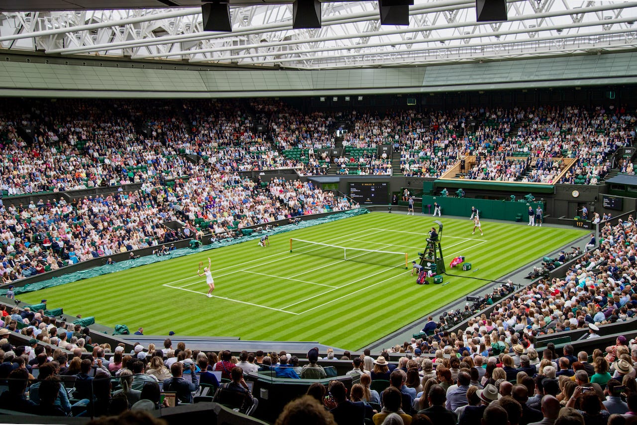 Match in progress on Centre Court at Wimbledon with the retractable roof closed and fourteen thousand spectators filling all three tiers