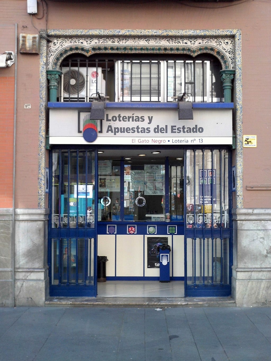 L'ingresso di un punto vendita ufficiale di Loterías y Apuestas del Estado: li riconosci per l'insegna e per gli infissi colorati di azzurro. L'ingresso di un punto vendita ufficiale di Loterías y Apuestas del Estado: li riconosci per l'insegna e per gli infissi colorati di azzurro.