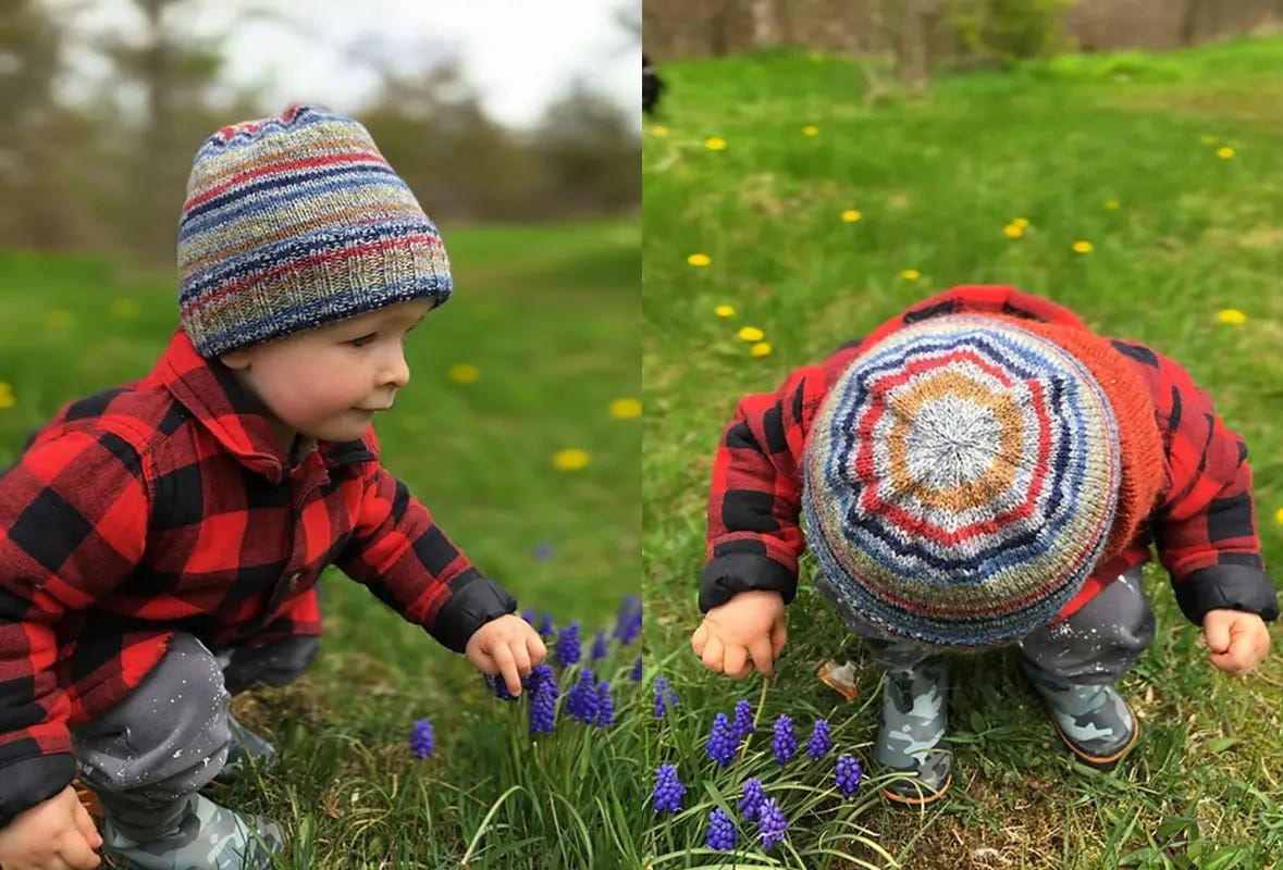 Toddler boy outside wearing a striped knit hat and wearing a red, buffalo plaid jacket.