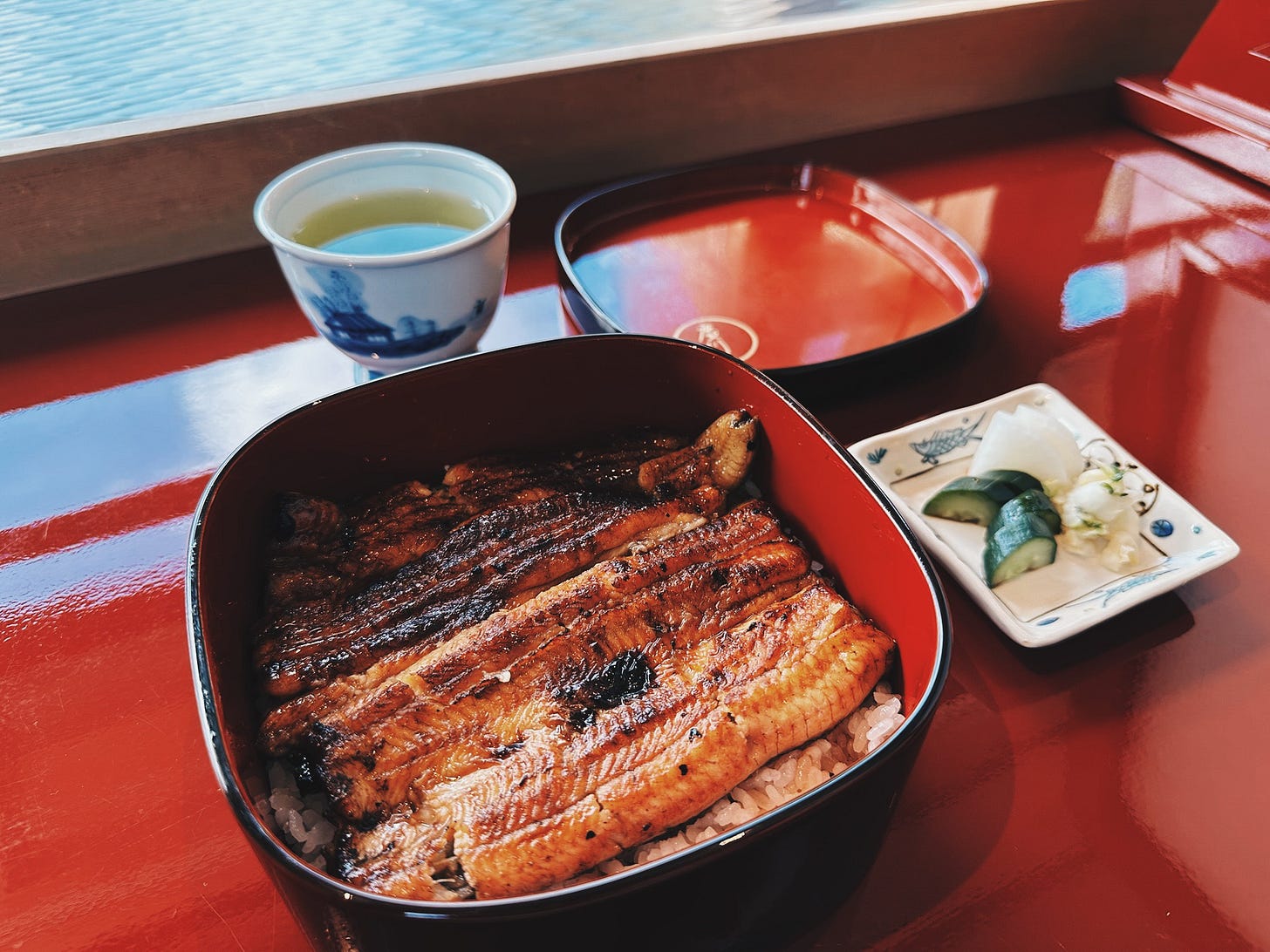 Traditional unagi don served in red lacquer box at Kyoto restaurant with green tea and pickles Traditional unagi don served in red lacquer box at Kyoto restaurant with green tea and pickles