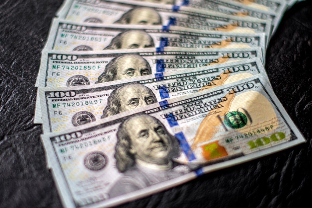 Close-up of several US 100 dollar bills featuring Benjamin Franklin, fanned out on a dark surface.
