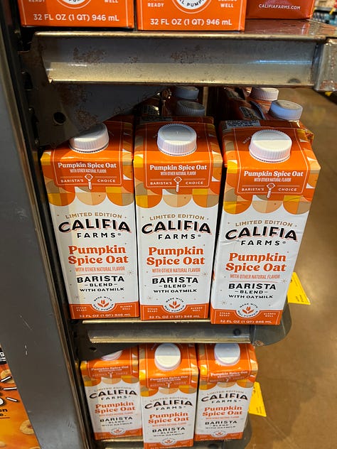 A grid of six photos of pumpkin-flavored products on shelves at an American Whole Foods: pumpkin spice grain-free cereal, pumpkin spice popcorn, pumpkin spice oat milk, cans of pumpkin chai hard tea, pumpkin spice oat bites and a pumpkin almond flour pancake mix.