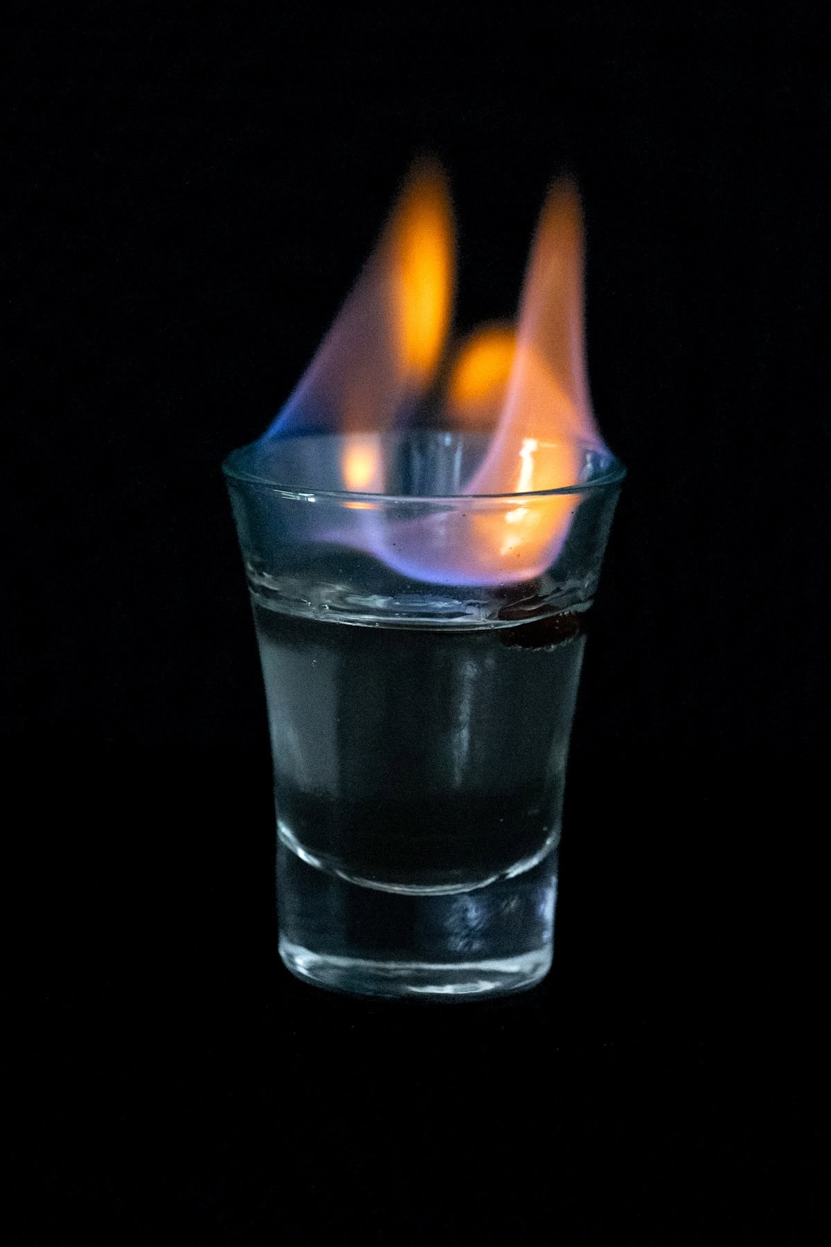 A Flaming Sambuca Shot on fire with an orange-blue flame, on a black background. A Flaming Sambuca Shot on fire with an orange-blue flame, on a black background.