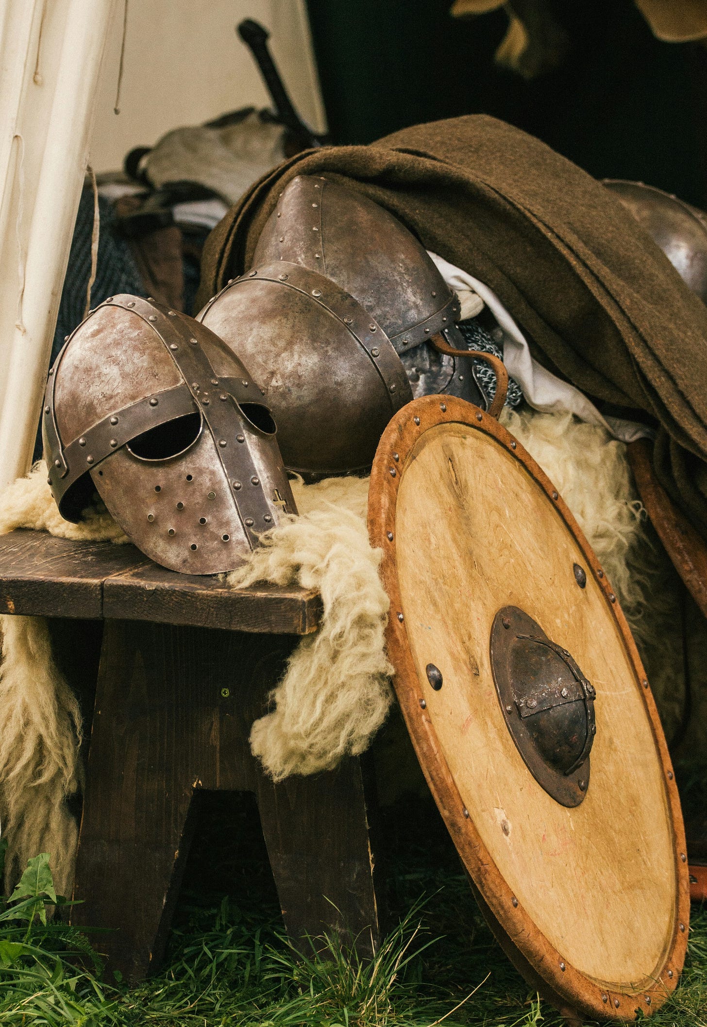 Medieval shield and metal face mask and body armor stacked on a bench.