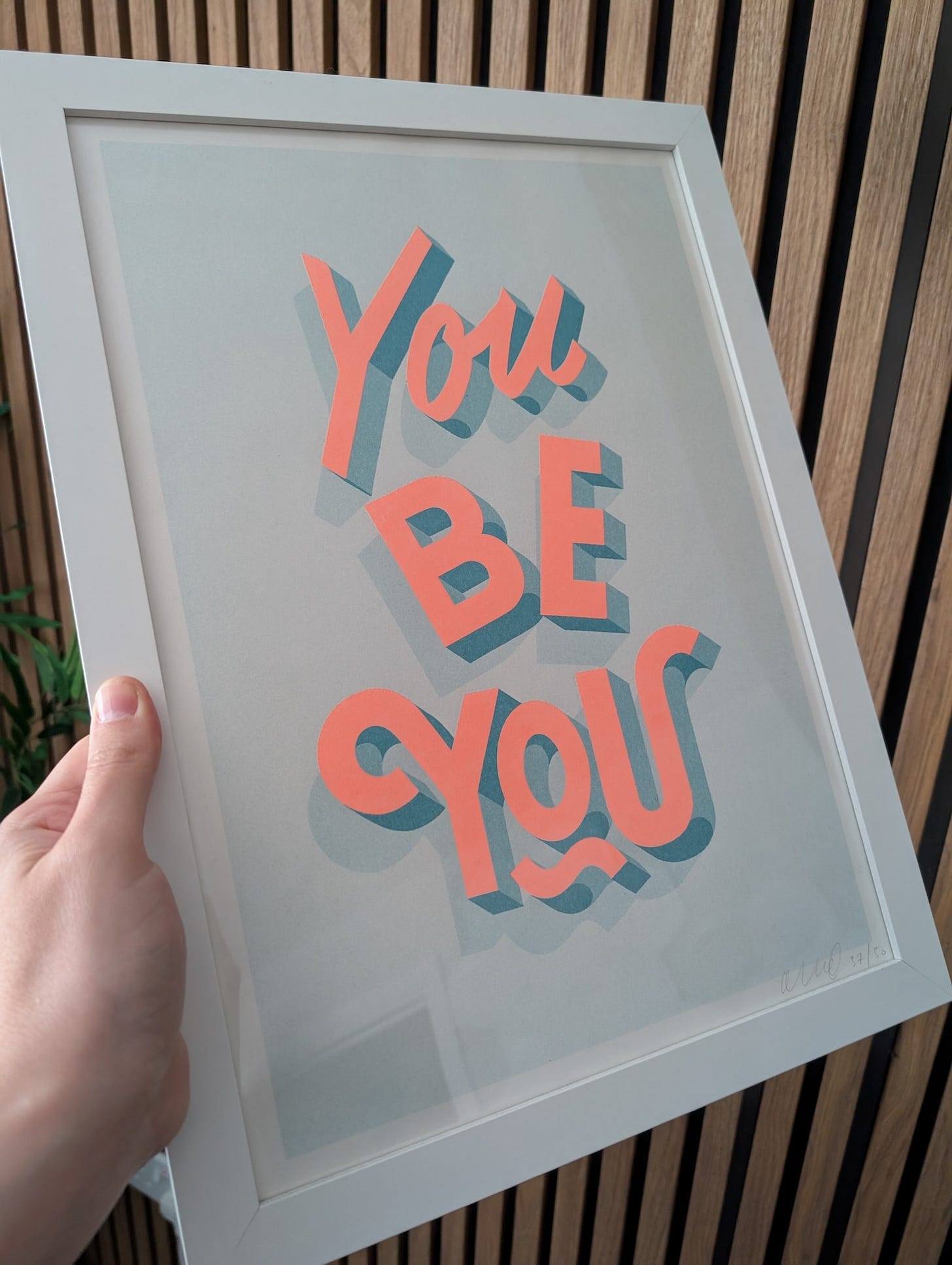 A print with a light blue background and luminous pink lettering saying 'you be you'