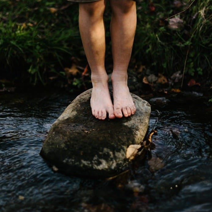 person standing on stone at center of body of water person standing on stone at center of body of water