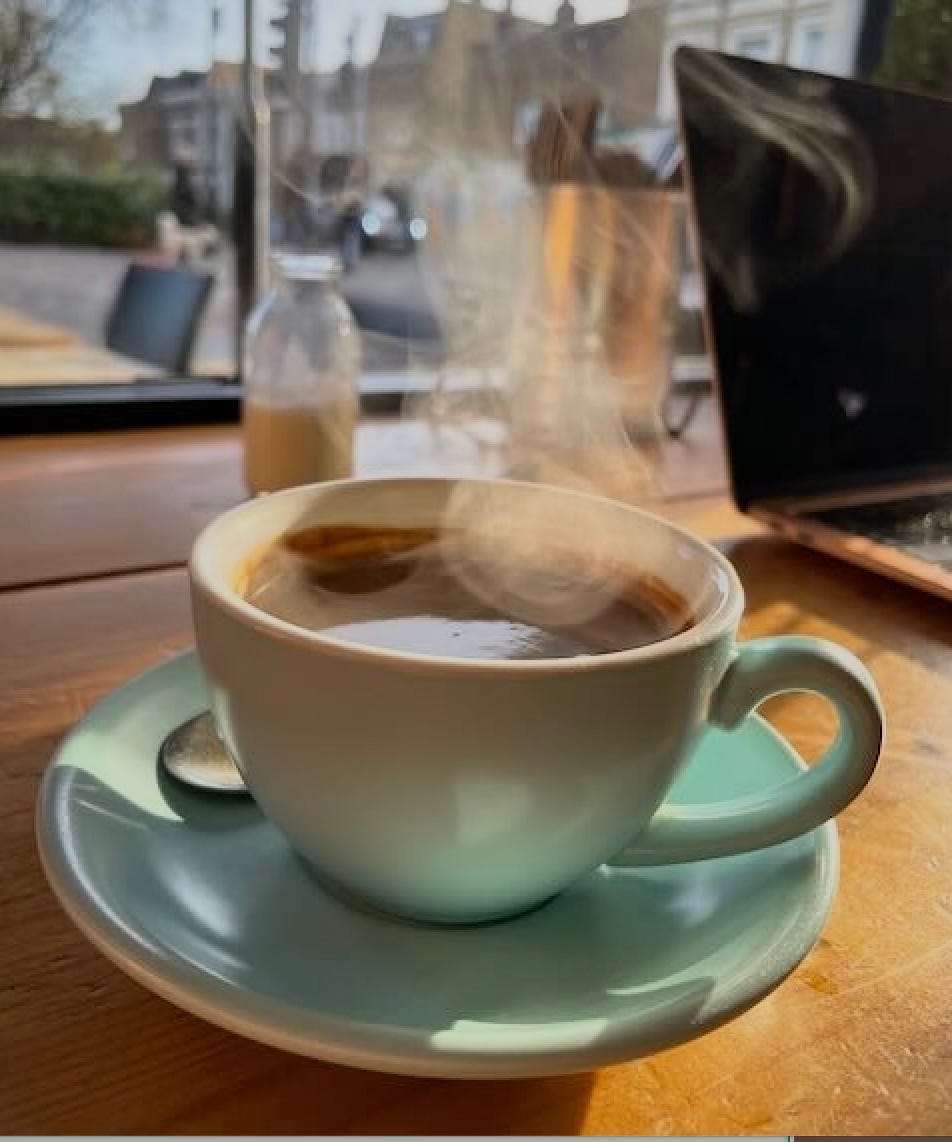 A teal cup of coffee and a laptop on a sunny cafe windowsill
