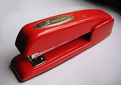 A small red stapler with the badge reading "Swingline" atop, seen from above on a white background with shadow at the top of the image A small red stapler with the badge reading "Swingline" atop, seen from above on a white background with shadow at the top of the image