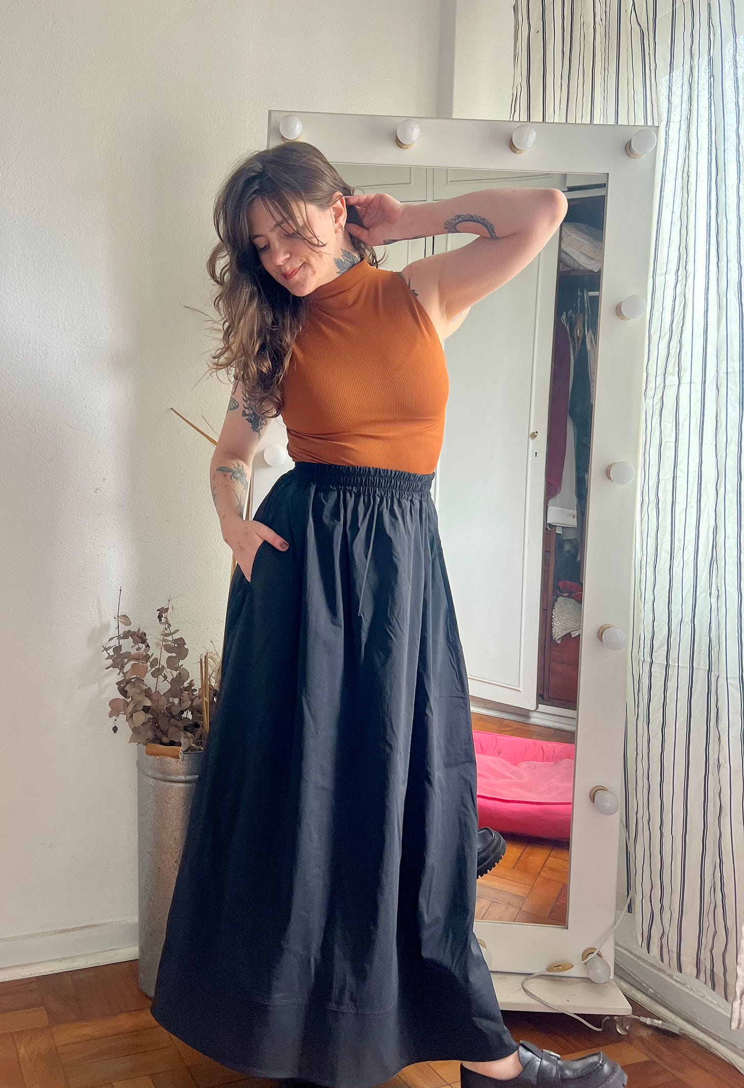 Euzinha de pé usando uma saia preta longa com uma mão no bolso, e uma regata de gola alta cor tijolo, tudo Insider